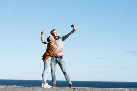Social media content creation concept. A happy couple recording themselves and vlogging in a sunny day at the seaside.の写真素材