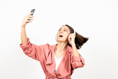 Happy latin woman with headphones dancing and taking a selfie over white background.の写真素材