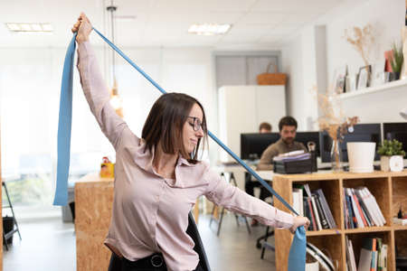 Healthy lifestyle in the workplace concept. Hispanic pretty woman stretching with a pilates rubber...