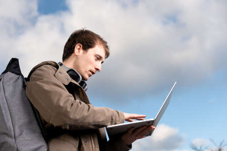 Closeup portrait of a handsome entrepreneur guy working on a laptop with the sky as background.