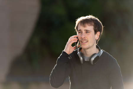 Closeup portrait of a handsome blond freelancer wearing headphones talking on the phone outdoors with a beautiful sunset light.の写真素材
