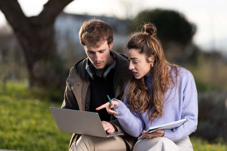 Young man and woman entrepreneurs working together on a laptop outdoors in a park with a beautiful sunset light.の写真素材