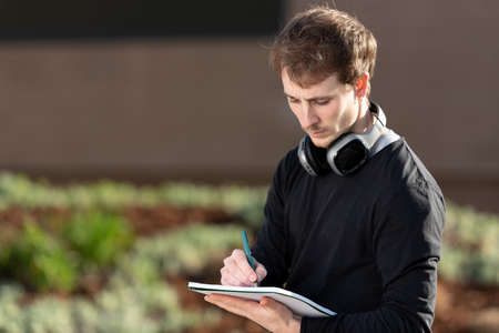 Young freelancer wearing headphones writing on a notebook outdoors in the park.の写真素材