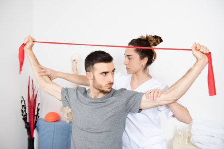 Physiotherapist helping to an athletic man to make rehabilitation exercises with a pilates rubber band.の写真素材
