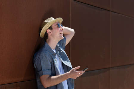 Happy young man laughing while holding a smartphone against a rusty metallic wall.