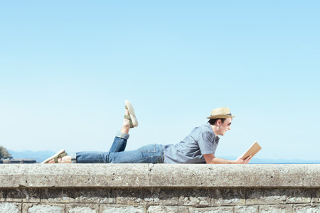 Laying happy man reading a book in summer