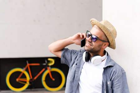 Hispanic confident man wearing a straw hat talking on the phone in front of a fixie bicycle.