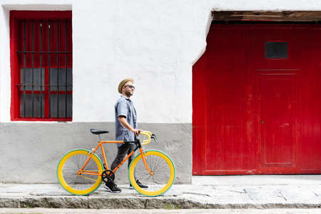 Happy hispanic man carrying a vintage bicycle at the old town of a city. Sustainable tourism concept.の写真素材