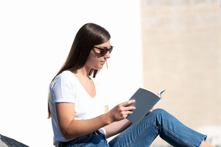 Closeup of a young female student reading a book outdoors.