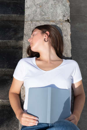 Young student sleeping and sunbathing with a book on her handsの写真素材