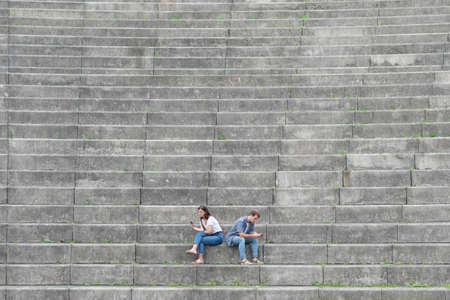 Digital and social media addiction with copy space. Young couple sitting on stairs ignoring each other and chating on the phone.の写真素材