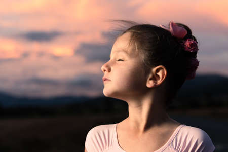 Dramatic portrait with closed eyes of a little ballerina child at sunset. Child dreaming her future concept.の写真素材
