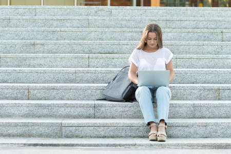 Concentrated young digital nomad working on her laptop sitting on the stairs.の写真素材