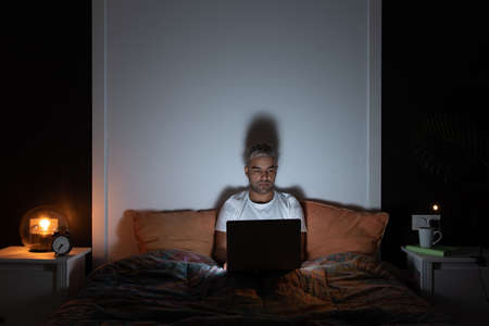 Freelance working from home concept. Hispanic man working on his laptop late at night sitting on his...