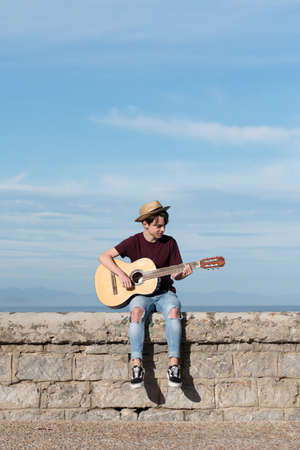 Cute teenage boy wearing a straw hat playing guitar outdoors.