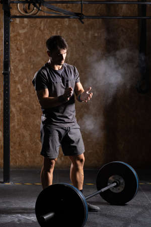 Concentrated weightlifter clapping hands with chalk before lifting a heavy barbell.