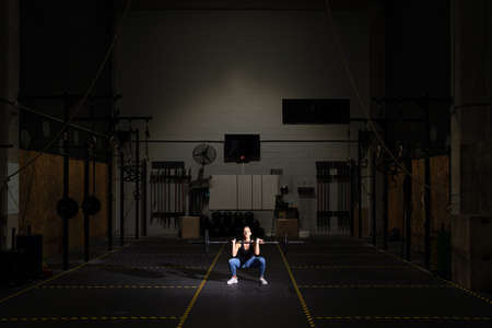 Fit woman training alone in a dark cross training gym. Determination and perseverance concept.の写真素材