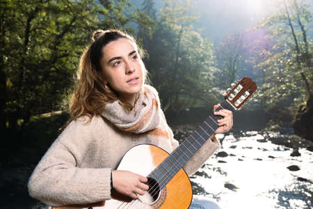 Young girl playing guitar outdoors, beside a river