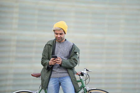Hispanic man using phone while resting on bicycleの写真素材