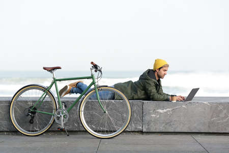 Hispanic digital nomad working on his laptop while laying beside bicycleの写真素材
