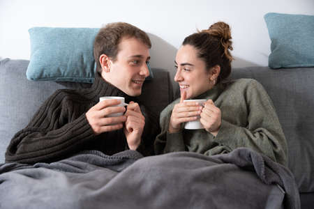 Romantic couple taking a cup of coffee and looking at each other while sitting on couchの写真素材