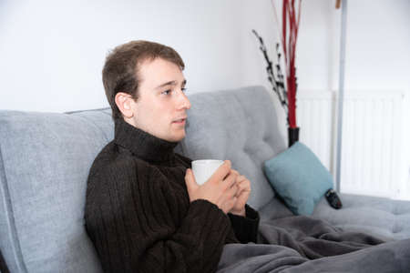 Young caucasian man holding a cup of coffee while sitting on couchの写真素材