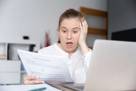 Desperate young freelancer looking at invoice in front of laptop
