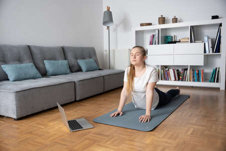 Young woman taking yoga virtual course at home.