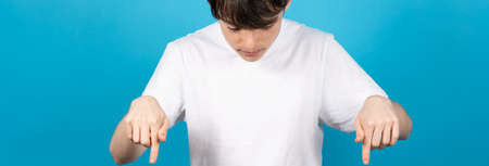 Teenager boy pointing down on blue background.