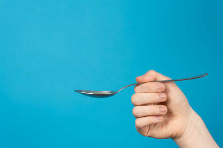 Hand holding spoon on blue backgroundの写真素材