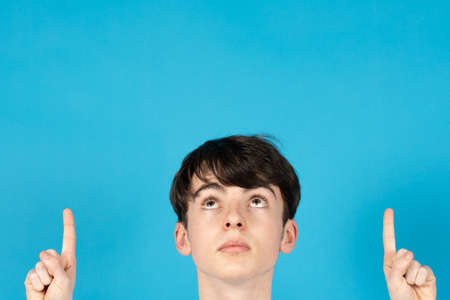 Handsome teenager boy pointing up and looking at blue copy space