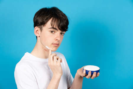 Teenager boy applying cream on face. Acne on puberty concept.