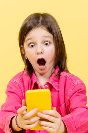 Shocked little girl looking amazed at phone. Parental control on internet concept.の写真素材