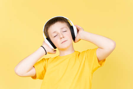 Cute boy listening relaxing music on headphones isolated on yellow backgroundの写真素材