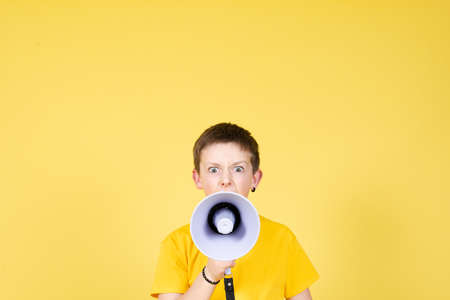 Angry boy speaking on megaphone looking straight to camera on yellow background with copy space.の写真素材