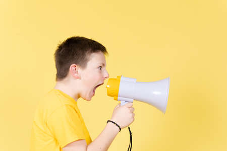 Angry boy shouting on loudspeaker to copy space on yellow background.の写真素材