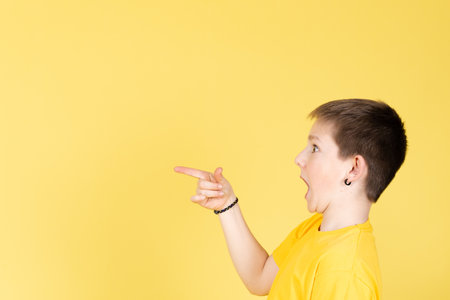 Surprised boy looking and pointing to copy space isolated on yellow background.の写真素材