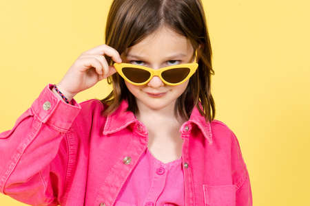 Arrogant little girl wearing sunglasses looking at camera isolated on yellow background