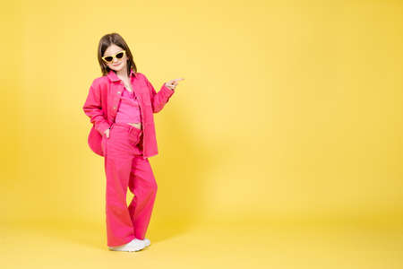 Cute little girl model posing and pointing at yellow copy space. Full body portrait of child wearing sunglassesの写真素材