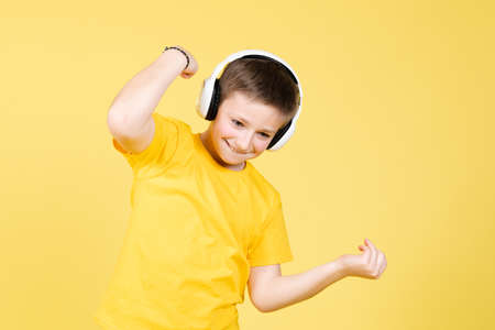 Cheerful positive boy listening to music and dancing isolated on yellow background.の写真素材