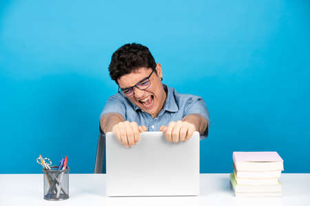 Angry hispanic student holding laptop isolated on blue background