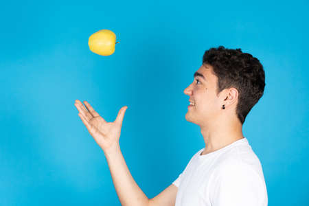 Hispanic young man throwing apple to air and playing with fruit isolated on blue backgroundの写真素材