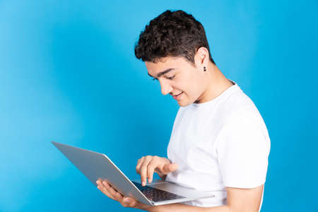 Hispanic young man typing on keyboard of laptop isolated on blue background.