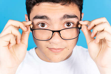 Hispanic teenager boy looking over glasses at camera isolated on blue background.の写真素材