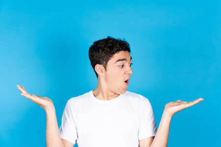 Hispanic teenager boy raising hands and looking to best choice with copy space isolated on blue background.の写真素材
