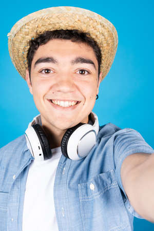 Smiling hispanic boy taking a selfie isolated on blue background.の写真素材
