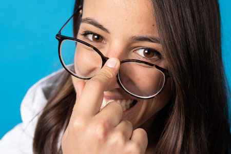 Happy pretty hispanic woman looking above eyeglasses at camera isolated on blue background.