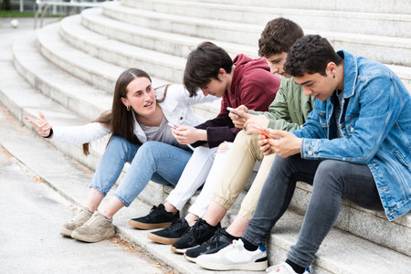Teenager girl asking for attention to group of friends concentrated on phones. Digital addiction and...