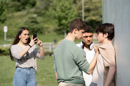 Two bullies threatening teenager boy and girl filming on phone. Cyber bullying and violence concept.の写真素材