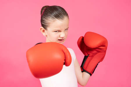 Little girl threatening and prepared to fight while looking at camera isolated on vivid pink background. Female stereotype concept. Child wearing boxing glovesの写真素材